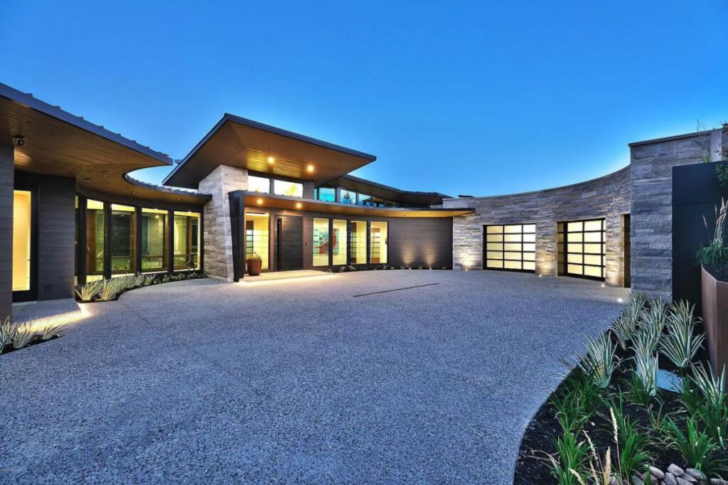 Contemporary single-story home with curved stone walls and courtyard at dusk