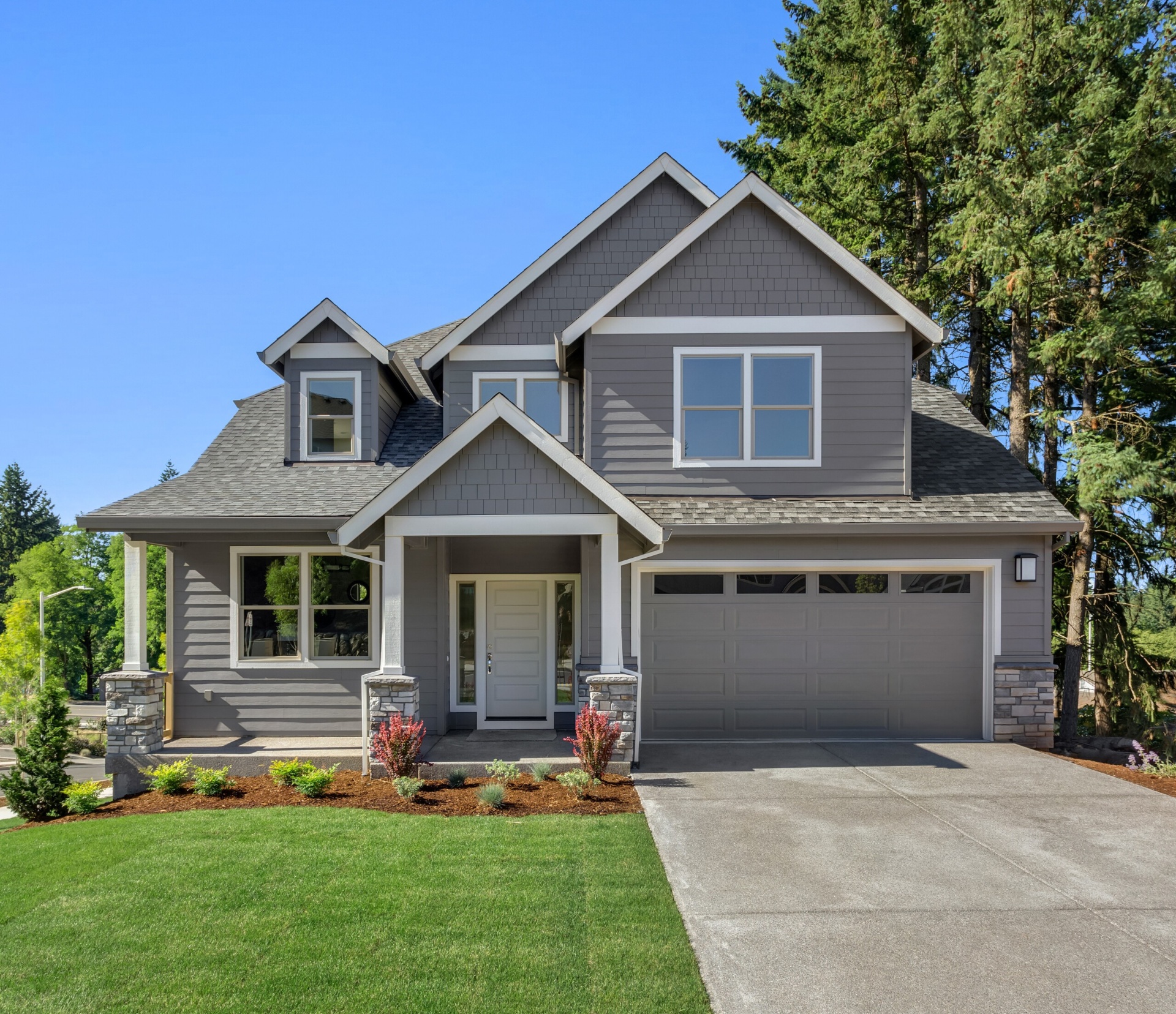 Two-story Craftsman home with gray siding, gabled roof, and stone column accents