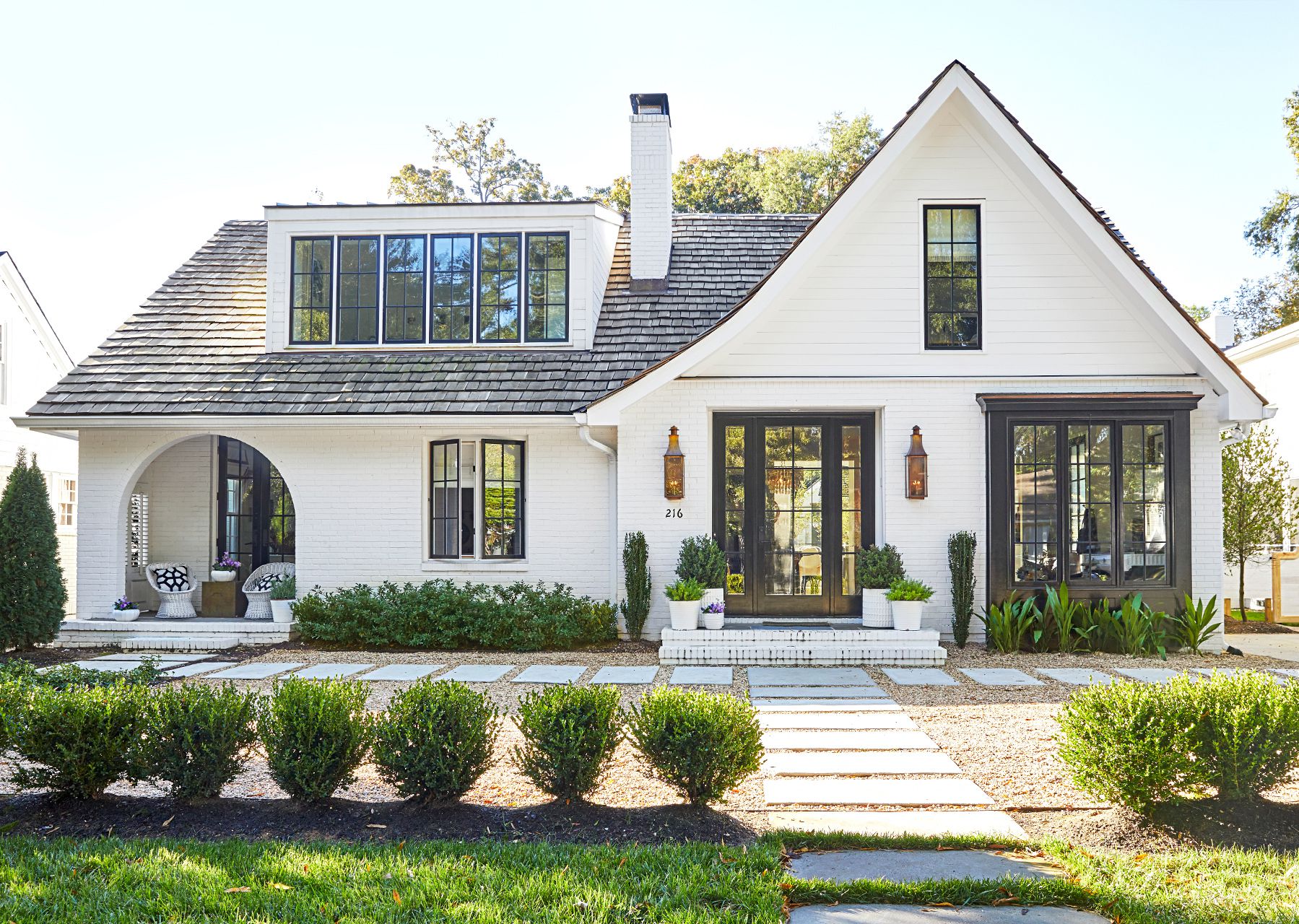 Modern white brick cottage with cedar shake roof, black-trim windows, and landscaped walkway