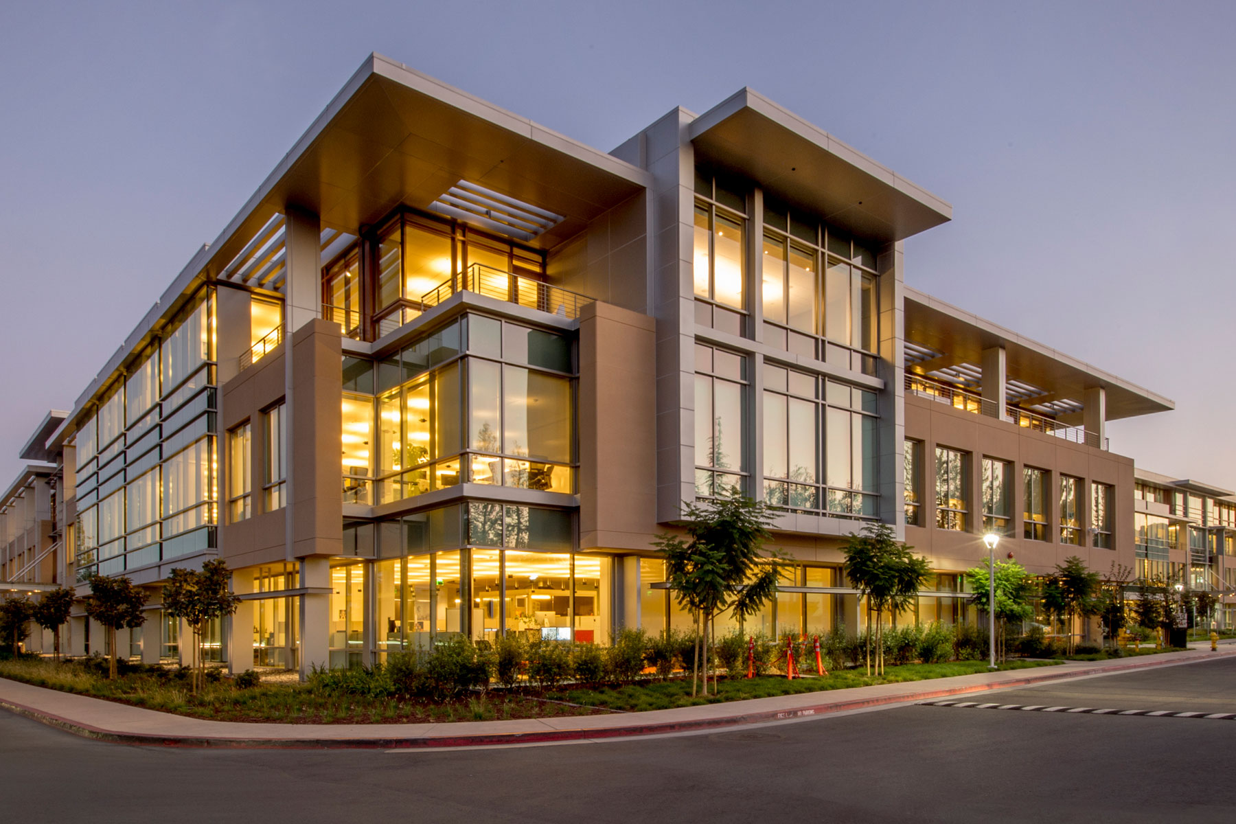 Modern multi-story office campus at dusk with warm interior lighting
