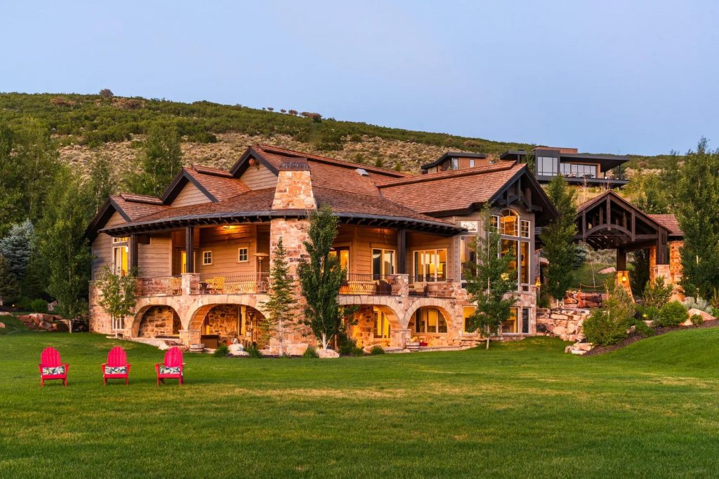 Timber and stone mountain lodge estate at dusk with red Adirondack chairs on the lawn
