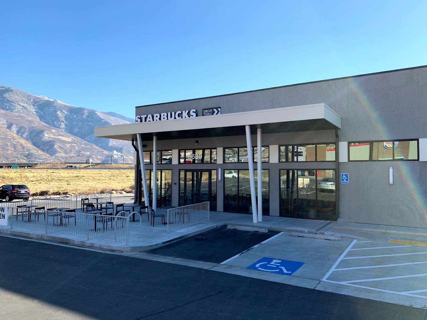 Modern Starbucks drive-thru building with mountain backdrop and rainbow