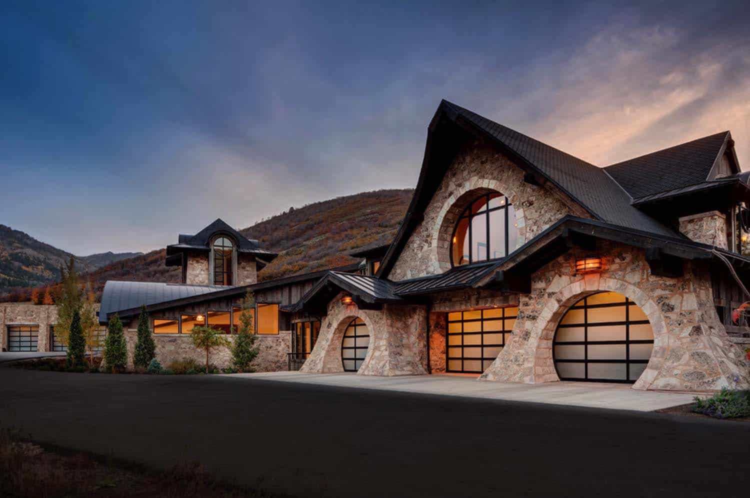 Custom stone mountain home with arched garage doors at sunset