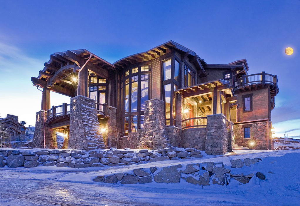 Heavy timber and stone luxury home illuminated at twilight with snow and full moon